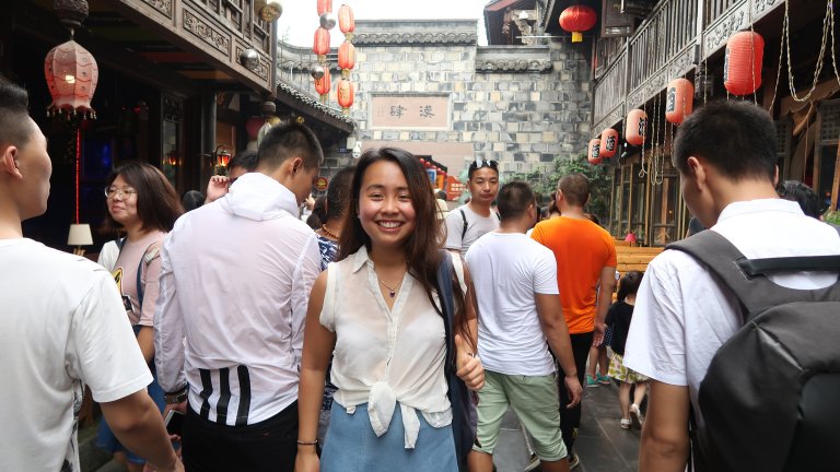 Student stands on street in Chengdu, smiling for camera