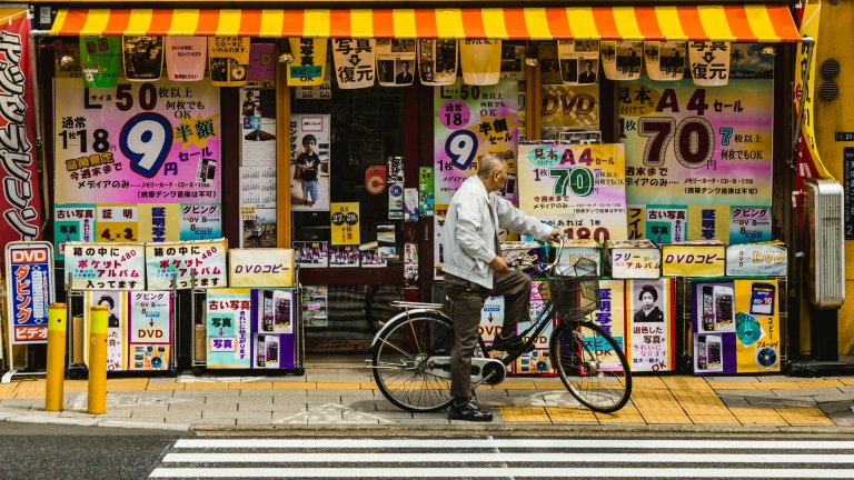 A man pauses on his bike in front of shop windows in Oshiage, Sumida, Japan